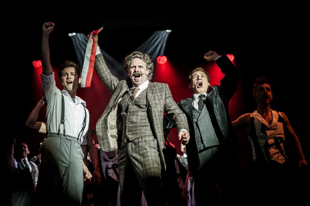 trzech mężczyzn śpiewa na scenie