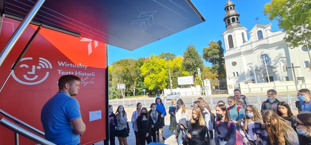 grupa oczekujących na wejście do Wirtualnego Teatru Historii "Niepodległa; w tle kościół