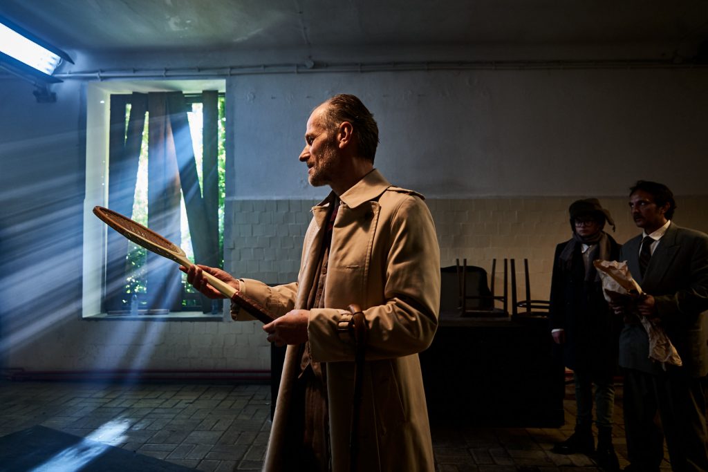 starszy mężczyzna trzyma w rękach rakietę tenisową we wnętru rudery