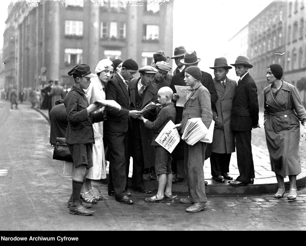 kolejka ludzi do osoby, która trzyma plik gazet