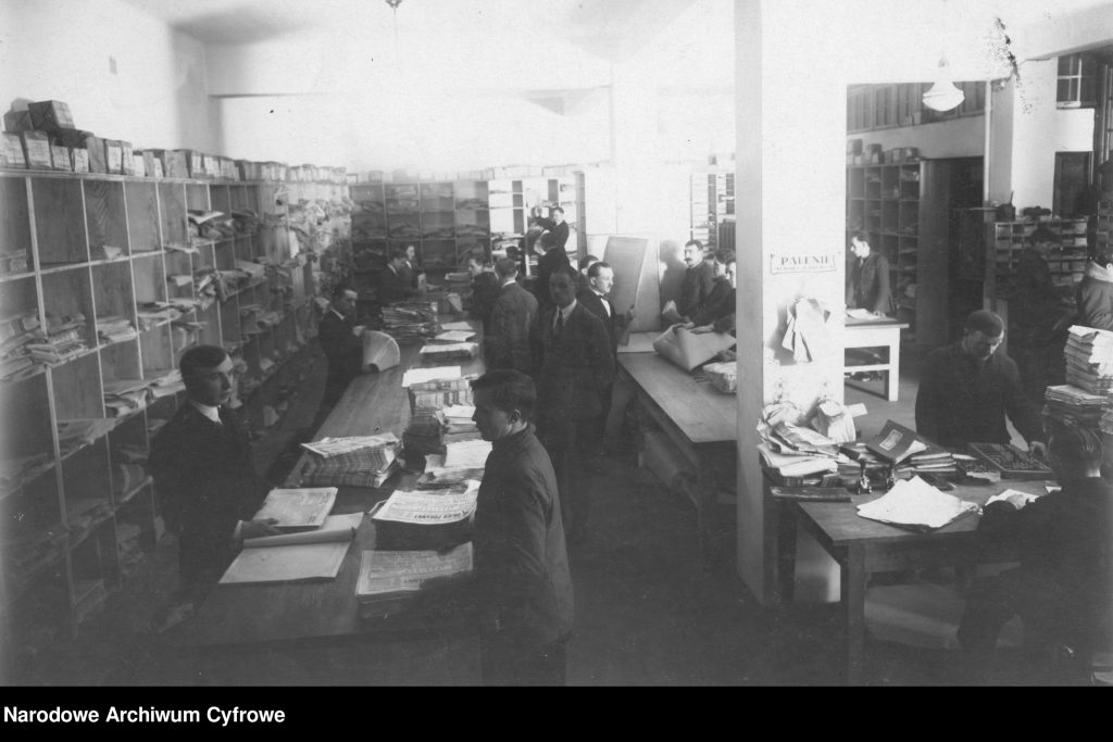 specyficzne wnętrze biuroe, między stołami kręcą się ludzie przy pracy