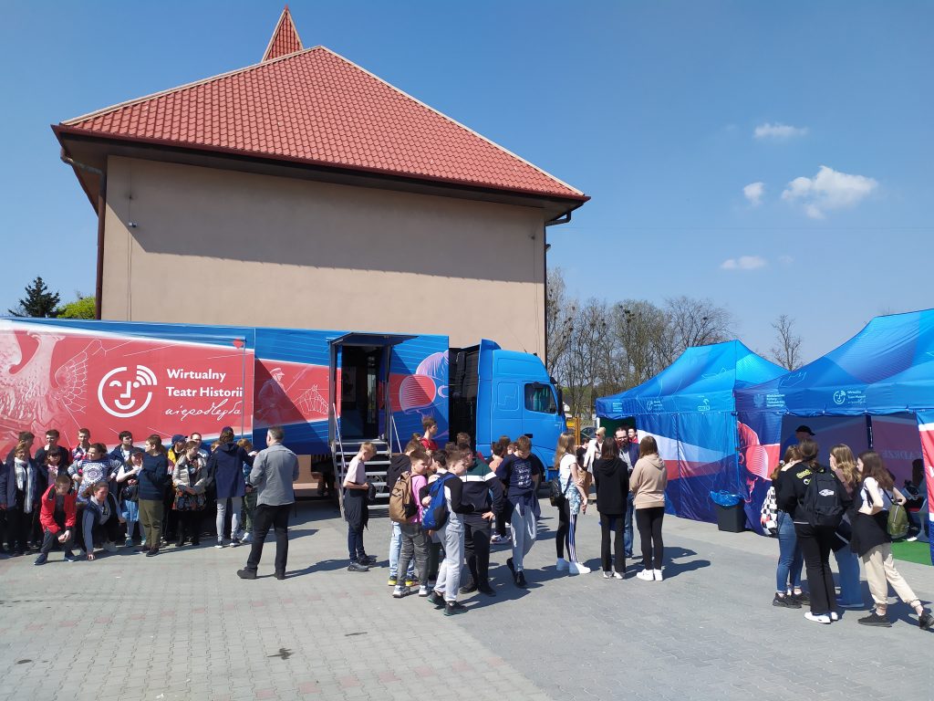 samochód Wirtualnego Teatru Historii w Działoszynie, w tle budynek i plac zabaw