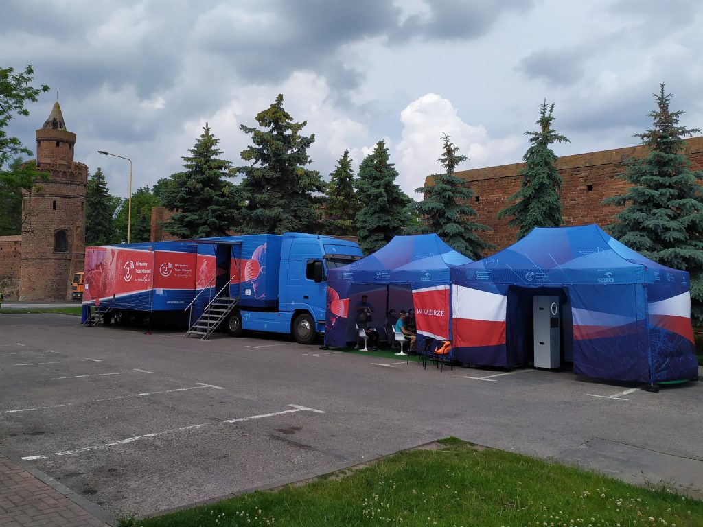 samochód Wirtualnego Teatru Historii na parkingu, w tle stare mury Pyrzyc