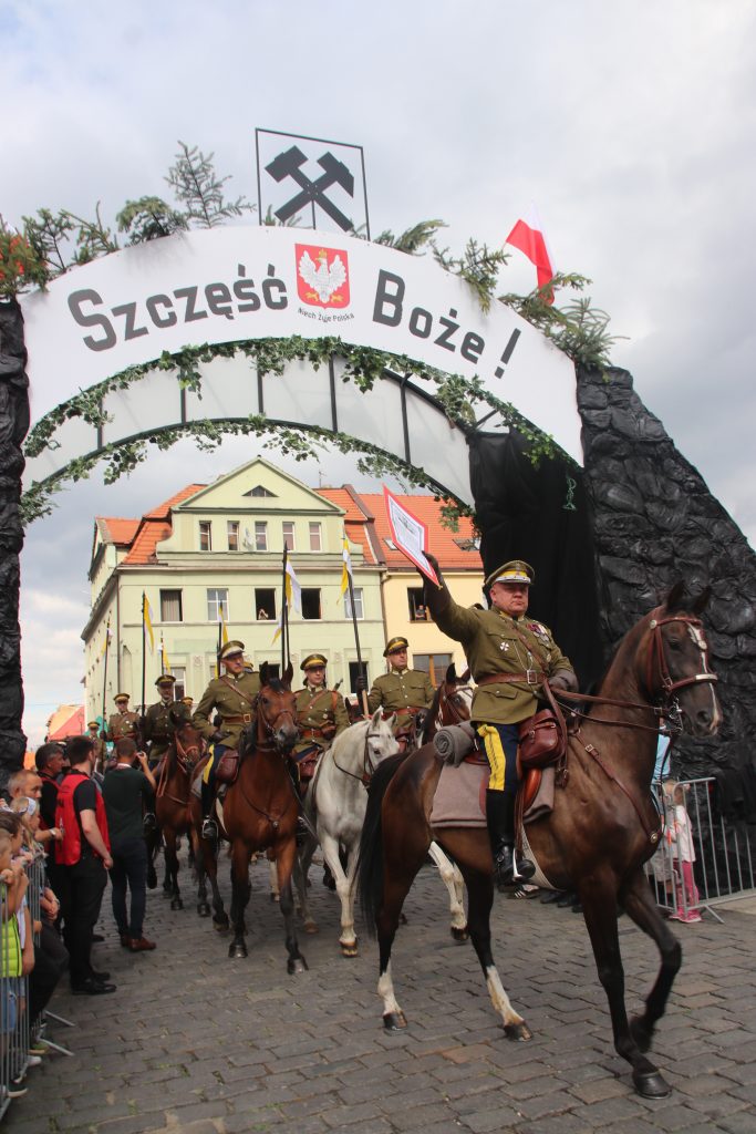 grupa rekonstrukorów w strojach żołnierzy przejeżdża na koniach przez zrekonstruowaną bramę