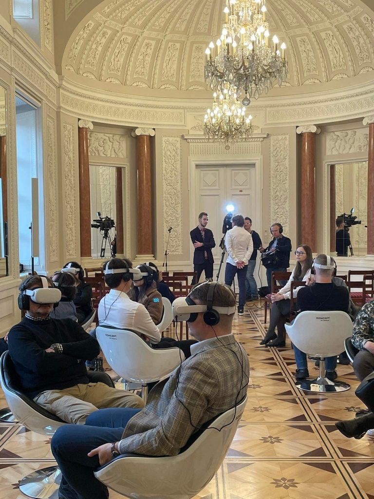 ludzie na obrotowych fotelach oglądają film VR, w tle nagrywany jest wywiad