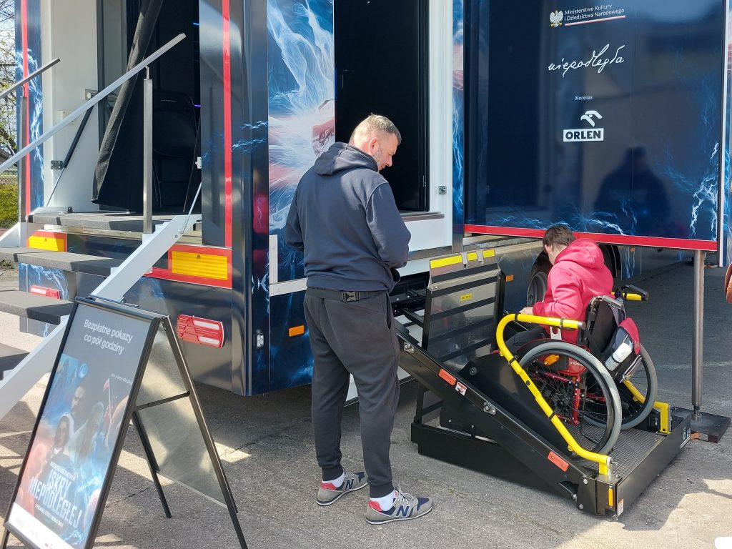 naczepa iskry niepodległej, na środku mężczyzna obsługujący windę, na platformie której znajduje się osoba na wózku inwalidzkim