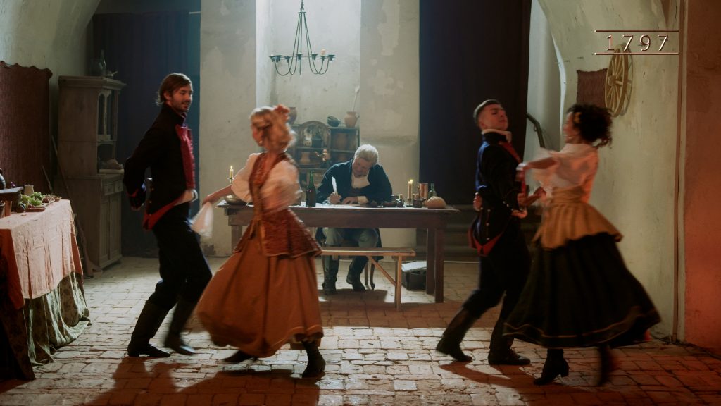 wnętrze gospody z XVIII wieku, na pierwszym planie dwie tańczące par, w tle mężczyzna pisze coś przy stole