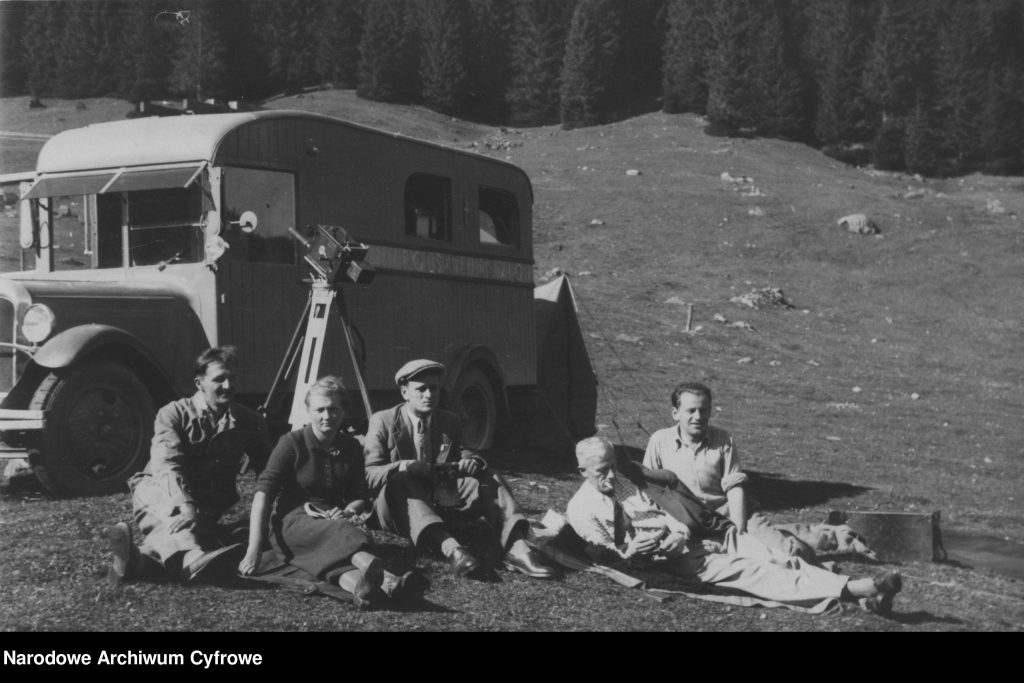 Członkowie ekipy filmowej Polskiej Agencji Telegraficznej oraz Polskiego Radia na polanie przed samochodem. Widoczna kamera.