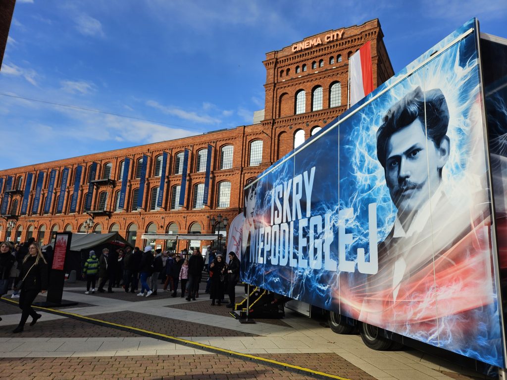 bok ciężarówki Iskry Niepodległej, za nim charakterystyczna architektura Manufaktury, przed wejściem zgromadzeni ludzie