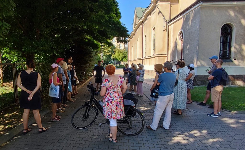 grupa ludzi słuchająca przewodnika, obok budowla architektoniczna