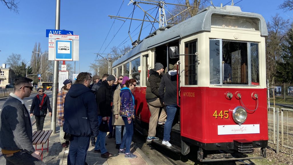 ludzie z przystanku tramwajowego wsiadają do zabytkowego wagonu