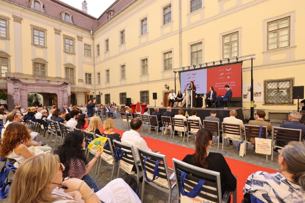 na dziedzińcu siedząca publiczność, z przodu scena gdzie przemawia Olga Wysocka na tle logo sezonu polsko-rumunskiego